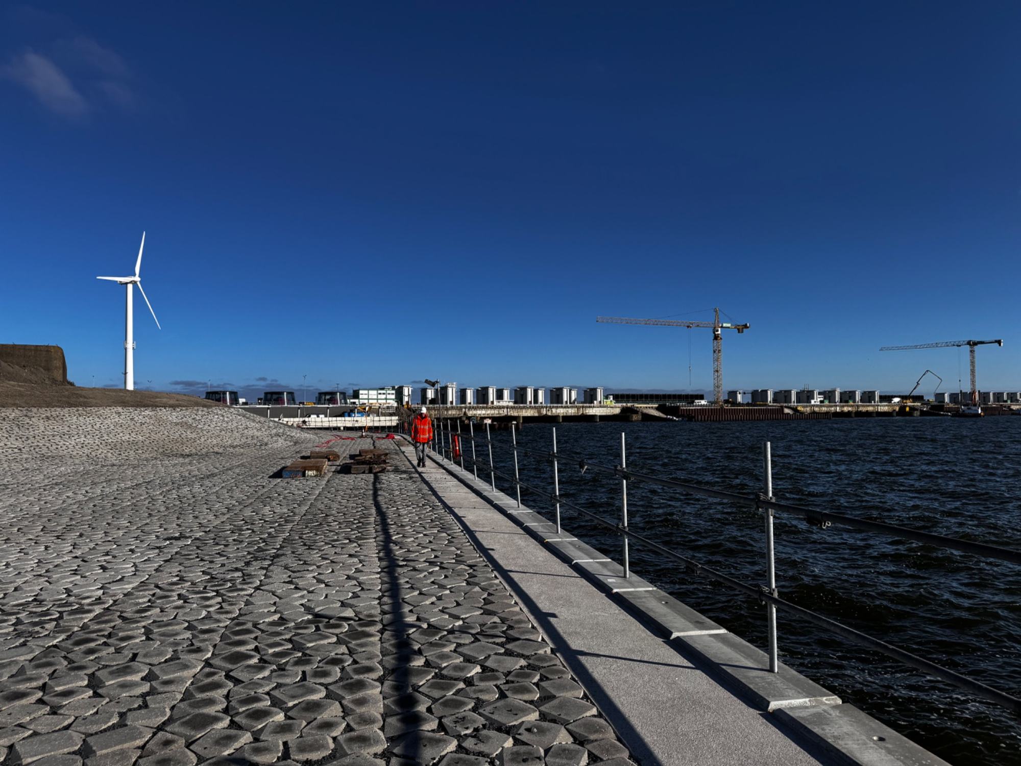 Wandelpad langs het water met op de achtergrond de sluizen van de Afsluitdijk en een windmolen onder een diepblauwe lucht